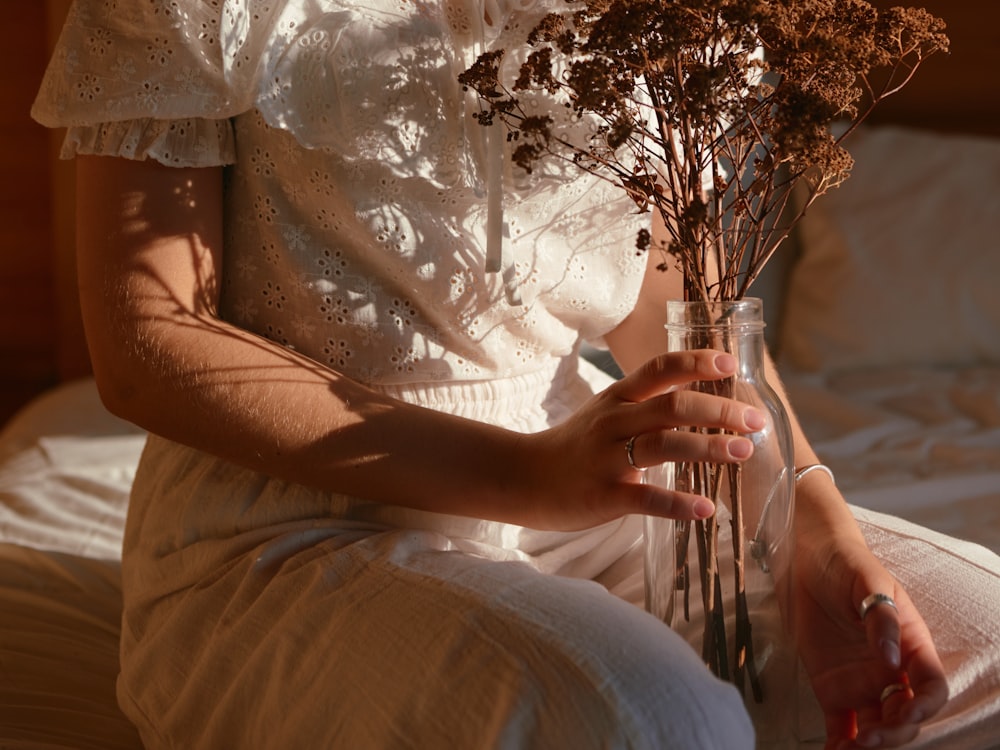 a woman sitting on a bed holding a vase filled with flowers