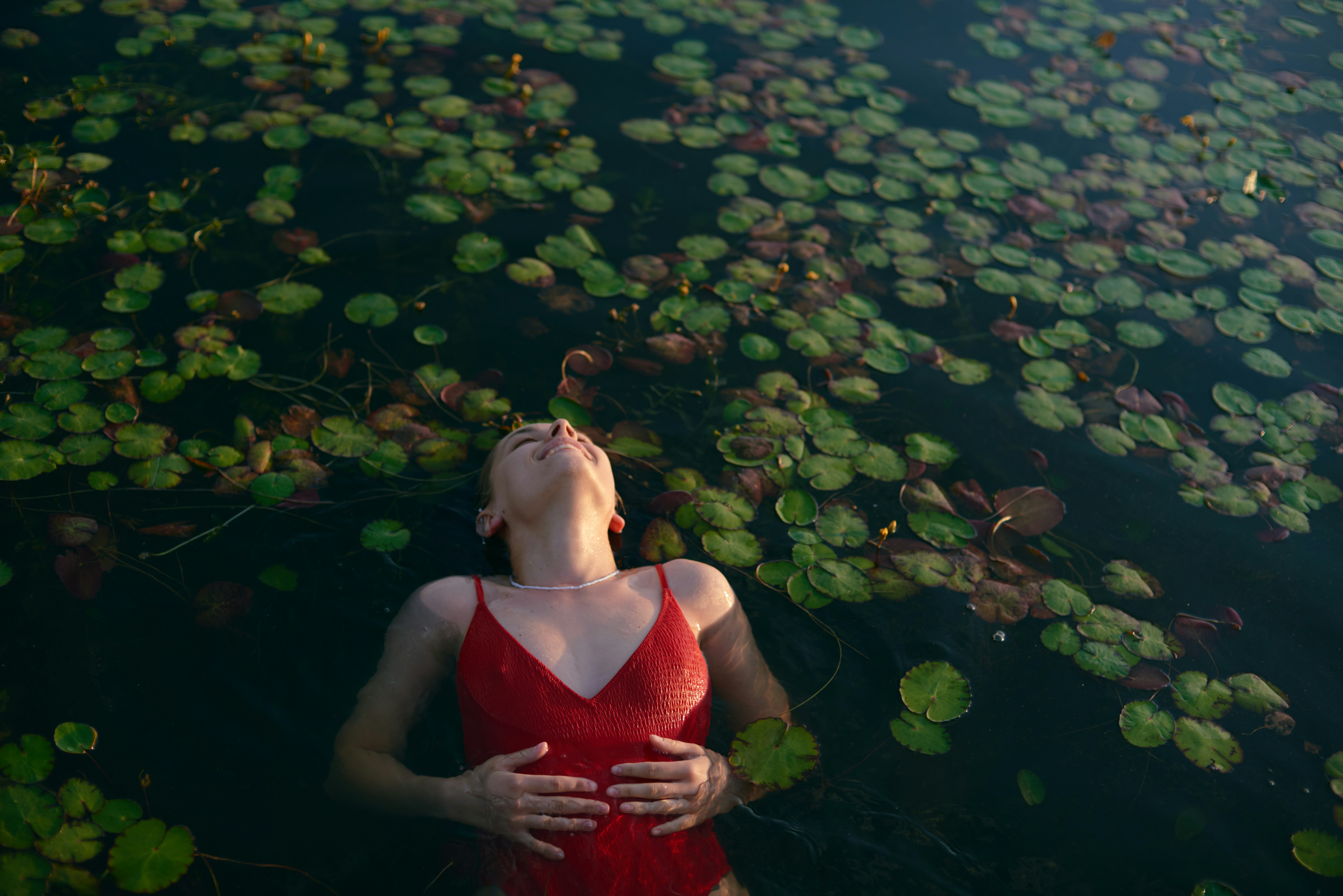 a woman floating in a body of water surrounded by lily pads, Portrait of a smiling woman floating on water with water lilies