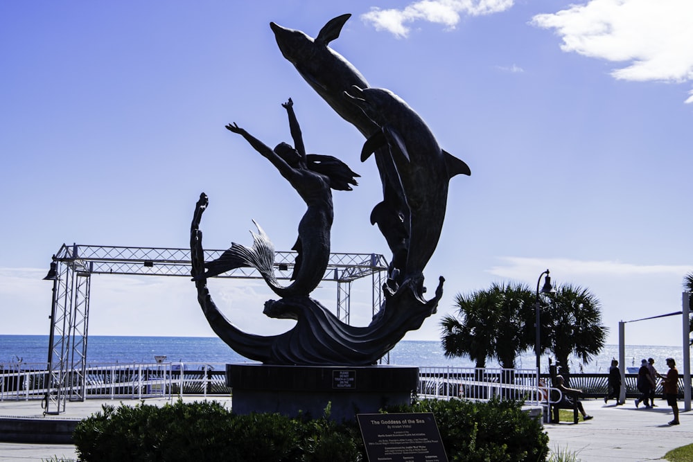 Eine Statue einer Frau, die einen Delfin vor dem Meer hält