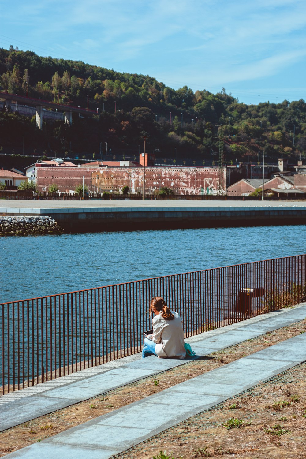 a woman sitting on a sidewalk next to a body of water