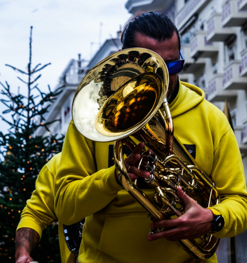 a man in a yellow hoodie is playing a trumpet