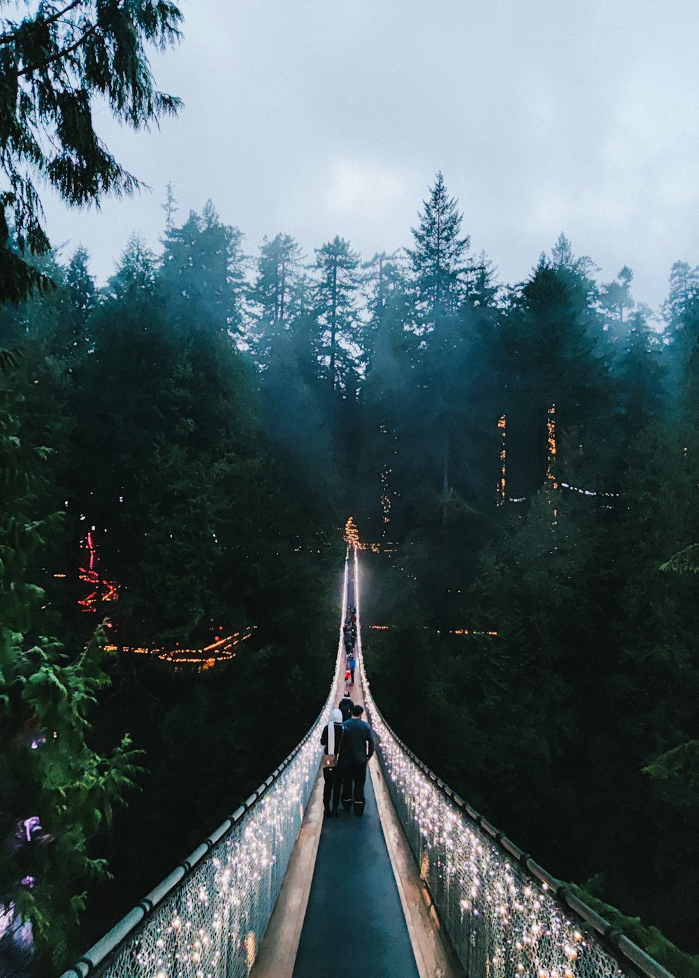 people walking across a bridge covered in christmas lights