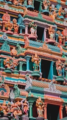 A beautifully intricate facade of a Hindu temple featuring numerous colorful sculptures depicting deities and mythical figures. The vibrant artwork is detailed with a variety of vivid colors, including teal, orange, pink, and yellow, showcasing traditional architectural elements and artistry.