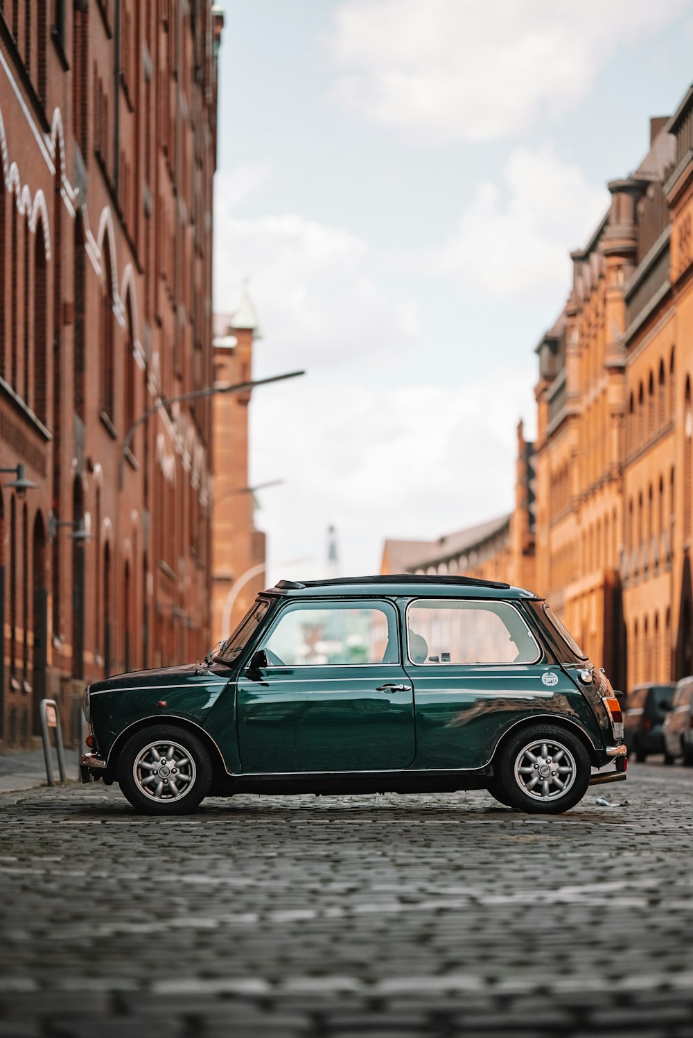 a small green car parked on a cobblestone street