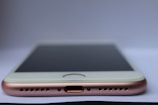 A close-up view of a smartphone lying flat on a surface with a focus on the bottom part of the device. Visible components include the charging port, speaker grills, and the edge of the screen. The phone has a metallic and sleek design.