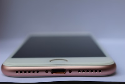 A close-up view of a smartphone lying flat on a surface with a focus on the bottom part of the device. Visible components include the charging port, speaker grills, and the edge of the screen. The phone has a metallic and sleek design.