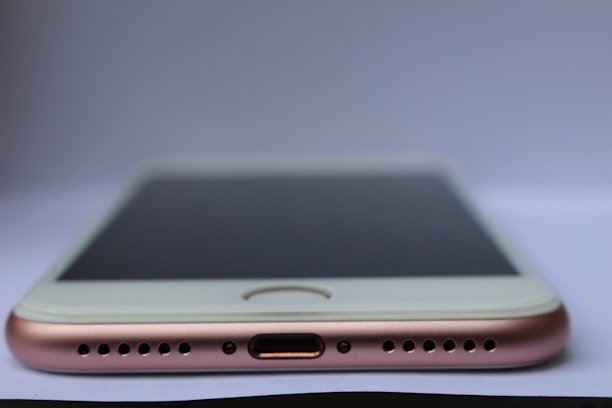 A close-up view of a smartphone lying flat on a surface with a focus on the bottom part of the device. Visible components include the charging port, speaker grills, and the edge of the screen. The phone has a metallic and sleek design.