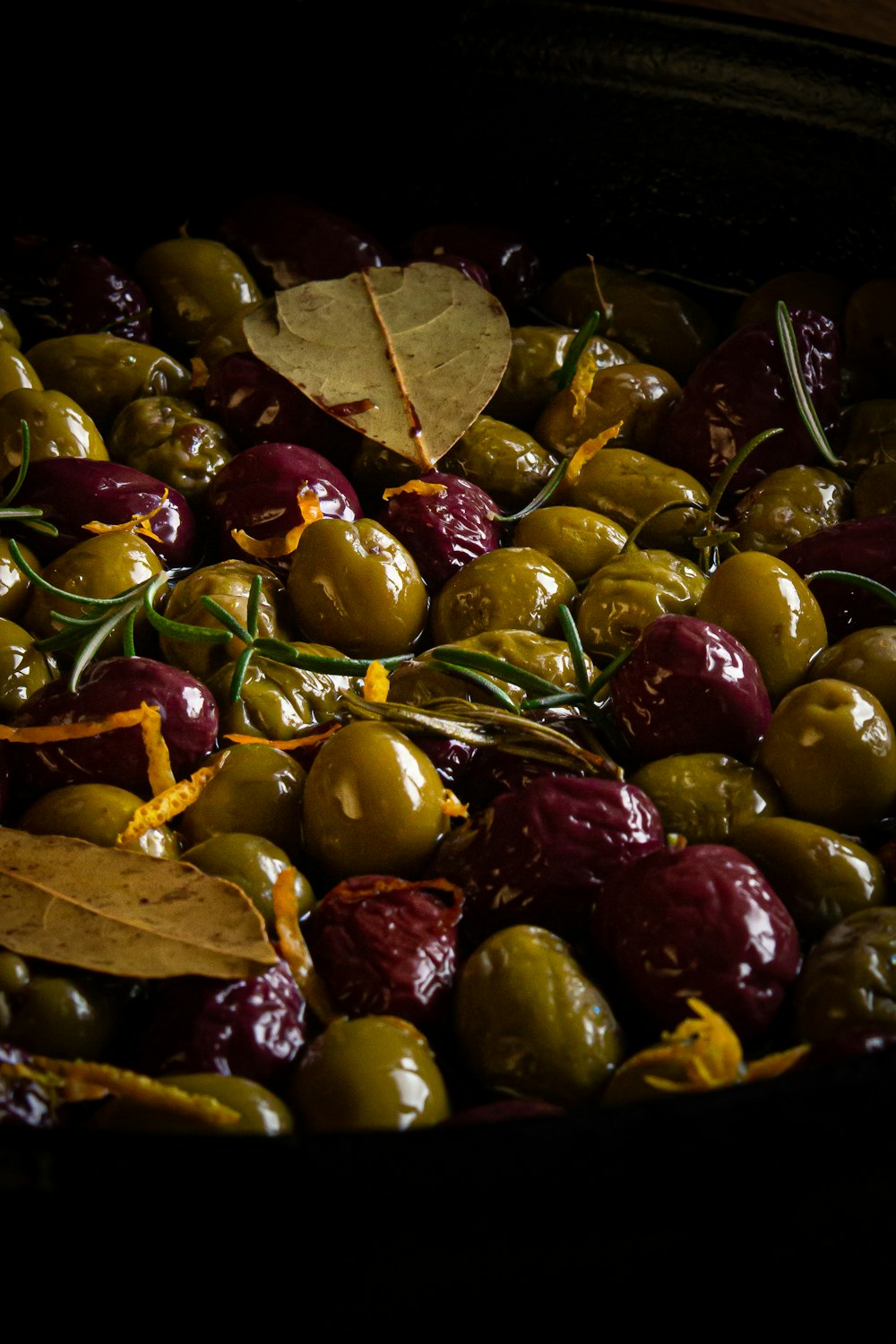 a bowl of green and red olives with a leaf on top