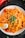 A plate of pasta topped with fresh herbs and a wedge of lemon. The pasta is mixed with chunks of vegetables and garnished with finely chopped greens.