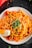 A plate of pasta topped with fresh herbs and a wedge of lemon. The pasta is mixed with chunks of vegetables and garnished with finely chopped greens.
