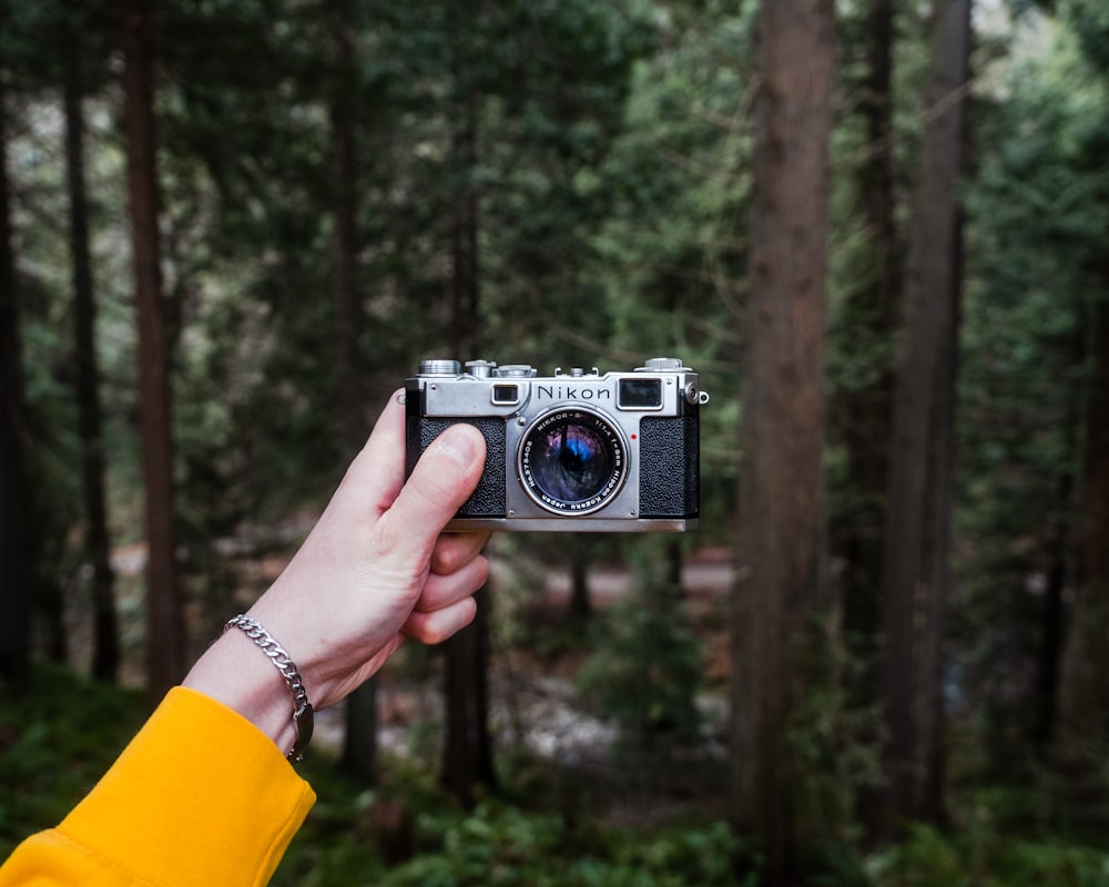 a person holding a camera in front of a forest