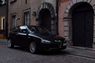 A sleek black VTC car parked in front of a historic French building at sunset.
