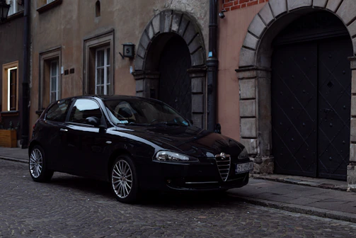 A sleek black VTC car parked in front of a historic French building at sunset.