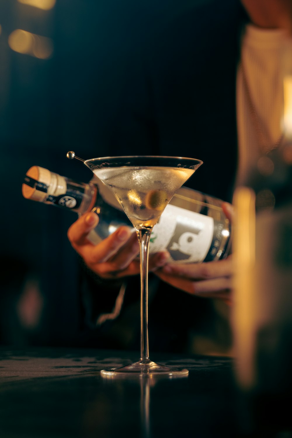 a person pouring a drink into a martini glass
