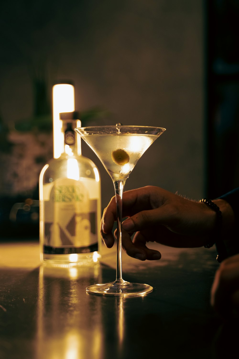 a person holding a martini glass in front of a bottle