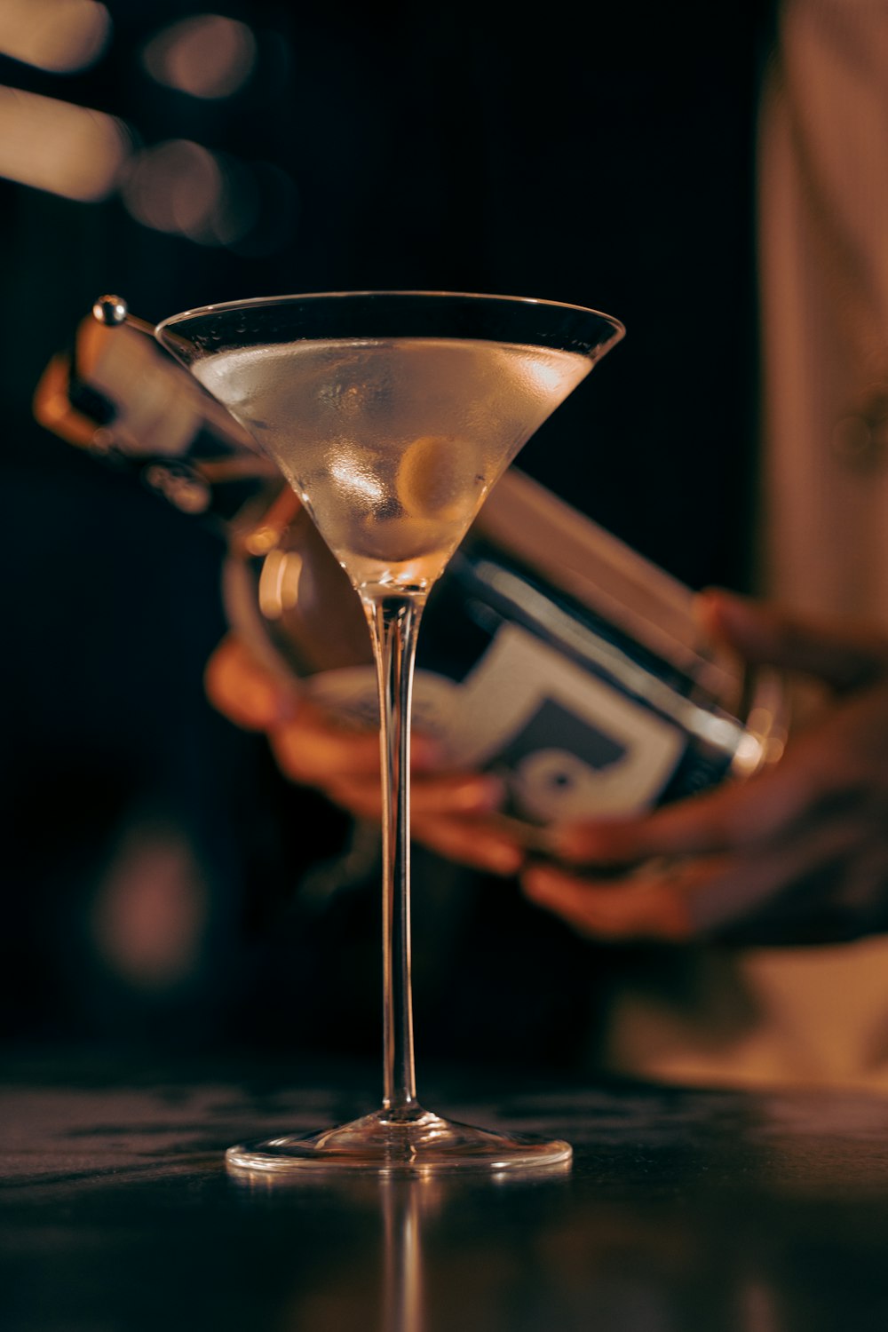 a person pouring a drink into a martini glass