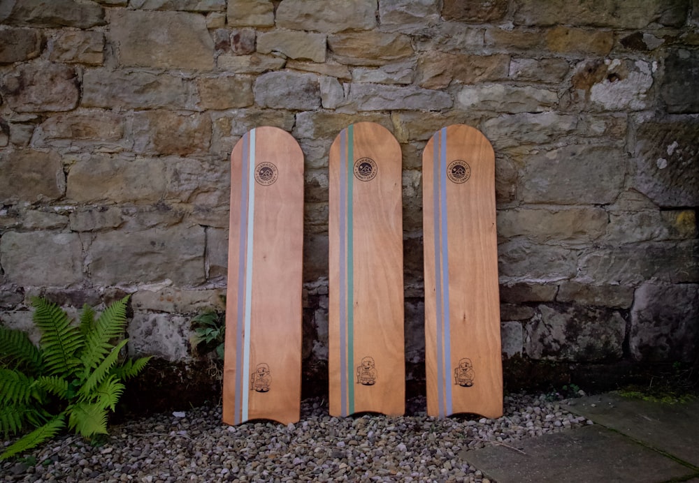 three wooden surfboards sitting next to a stone wall