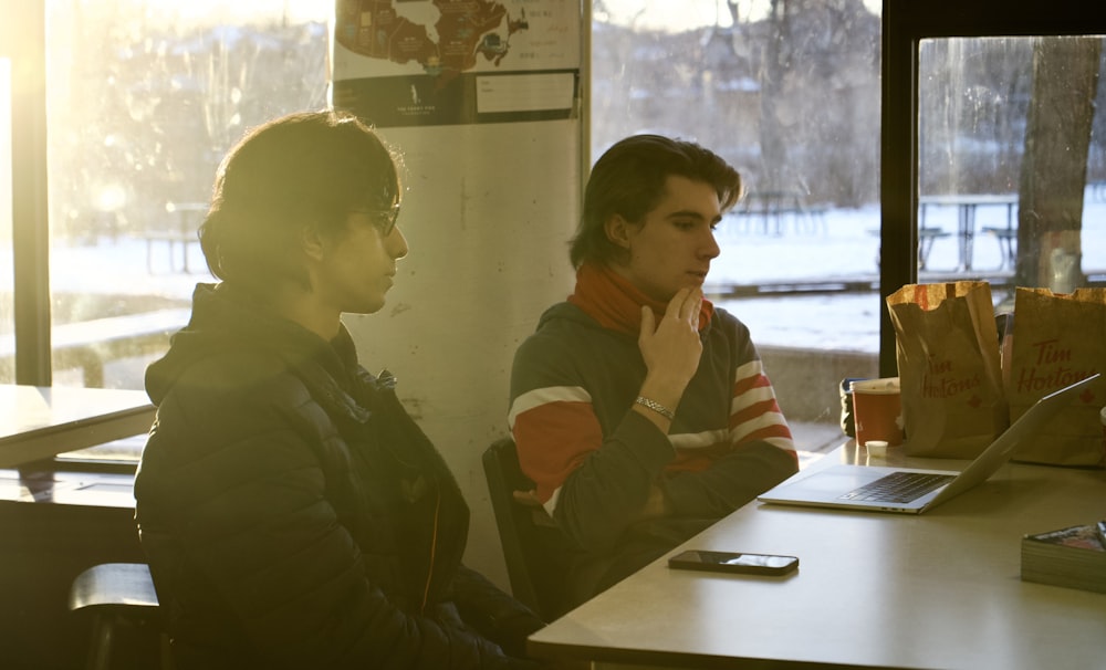 two people sitting at a table in front of a laptop computer