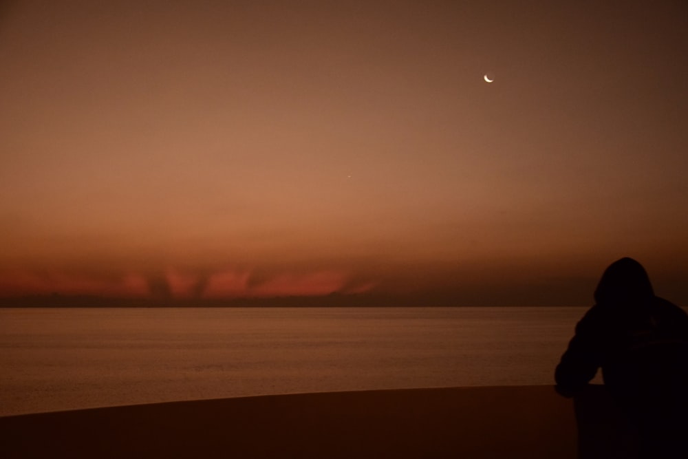 Una persona parada en una playa viendo la puesta de sol