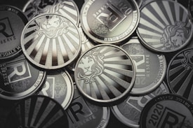 A collection of silver coins featuring a lion's head surrounded by sunburst rays and inscriptions such as 'Scottsdale', '1 TROY OZ', and 'RESERVE'. The design elements are embossed and the coins are metallic and reflective.