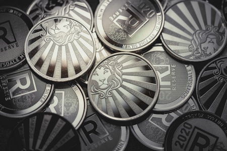 A collection of silver coins featuring a lion's head surrounded by sunburst rays and inscriptions such as 'Scottsdale', '1 TROY OZ', and 'RESERVE'. The design elements are embossed and the coins are metallic and reflective.