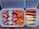 Various processed foods are arranged in two containers. On the left, there are pink, star-shaped pieces and round pink and white pieces with stars in the center. On the right, there are sausages and breaded skewers.