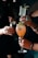 Several hands holding different types of cocktails; one glass is tall with a sprig of mint, another is in a rounded goblet with an orange-hued drink, and another is a short glass with a dark appearance and garnished with berries. The scene suggests a social gathering or celebration.