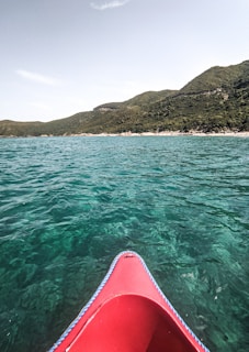 A vibrant kayak gliding through the crystal-clear waters of Samaná Bay at sunrise, surrounded by lush green hills.