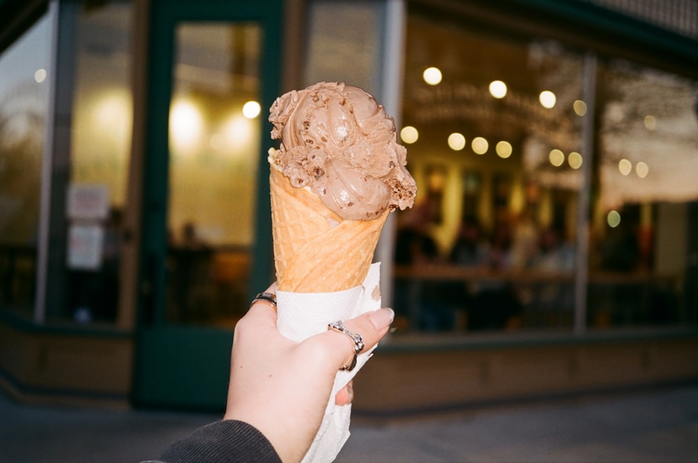 a person holding up an ice cream cone in front of a building