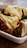 A dish featuring what appears to be stuffed dumplings or wraps covered with melted cheese. The filling is visible, showing cooked meat or vegetables, and garnished with chopped green onions. The food is served in a rectangular white dish placed on a wooden surface.
