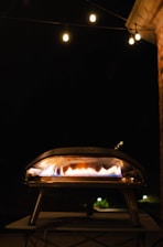 A sleek black and red automated pizza oven glowing warmly in a modern urban setting at dusk.