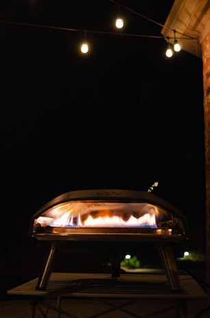 A sleek black and red automated pizza oven glowing warmly in a modern urban setting at dusk.