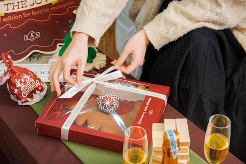 Hands carefully wrapping a chocotone in festive red and gold paper with a shiny ribbon