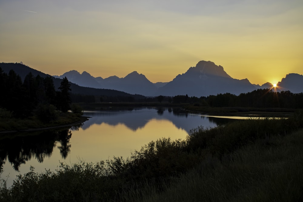 the sun is setting over a mountain lake