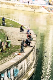 Anglers sharing tips and equipment by a calm riverbank in military green attire.