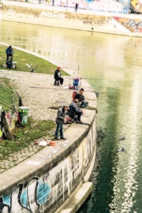 Anglers sharing tips and equipment by a calm riverbank in military green attire.