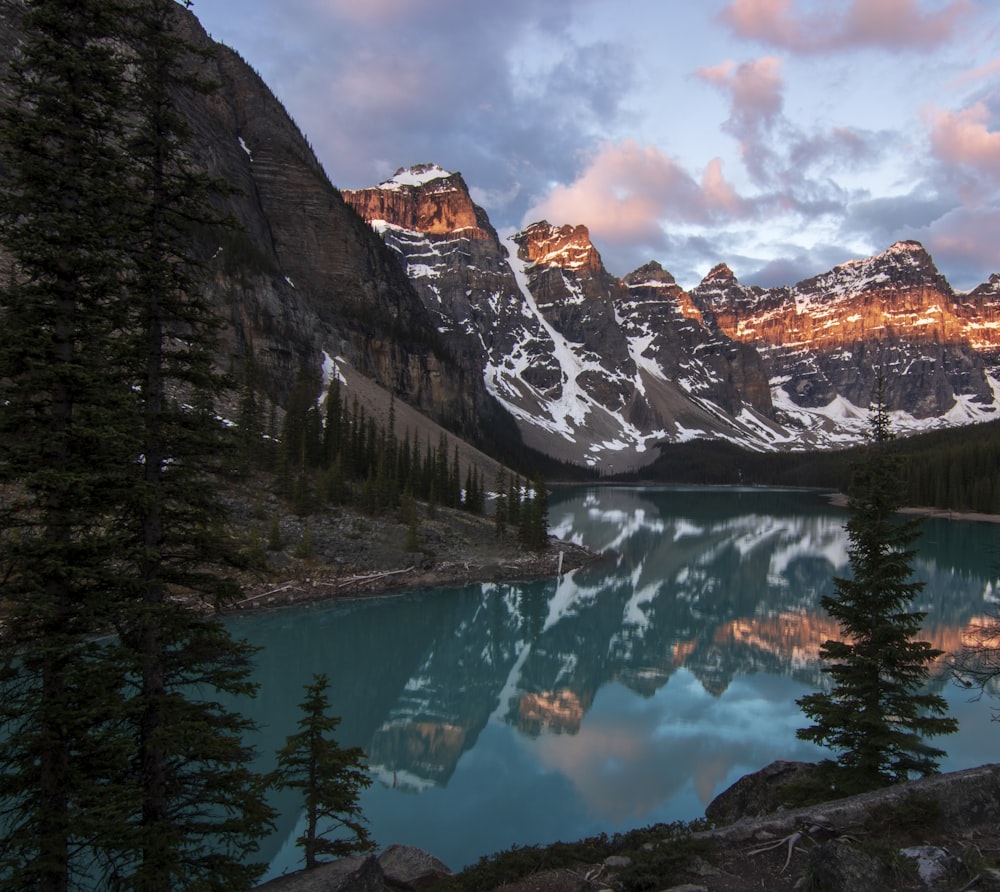 a lake surrounded by mountains and trees under a cloudy sky