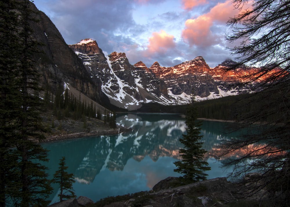 a lake surrounded by trees and mountains under a cloudy sky