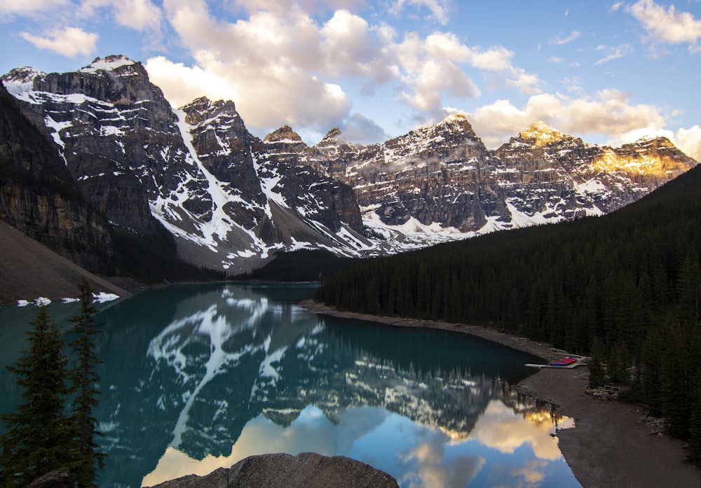 a lake surrounded by snow covered mountains under a cloudy sky