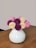 A close-up photo of a minimalist ceramic vase holding fresh wildflowers on a wooden table.