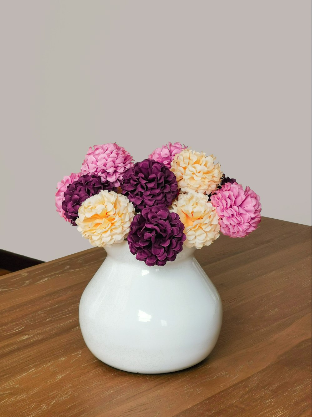 a white vase filled with colorful flowers on top of a wooden table