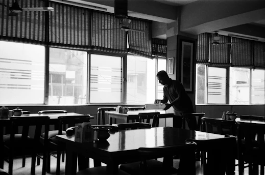 A cleaner wiping down tables in a cozy, softly lit restaurant dining area.
