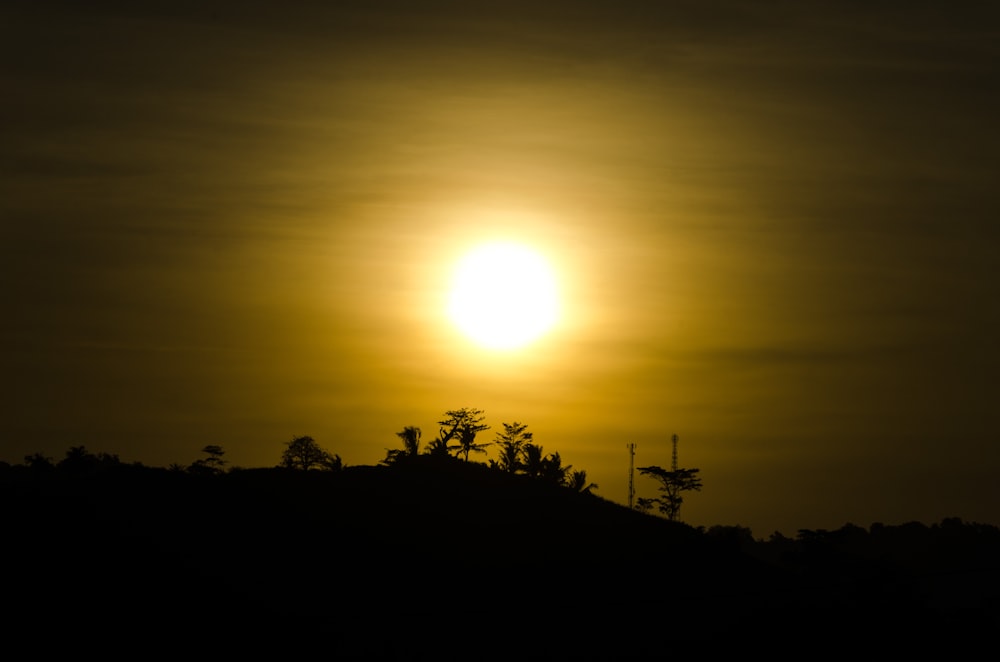 the sun is setting over a hill with trees on it