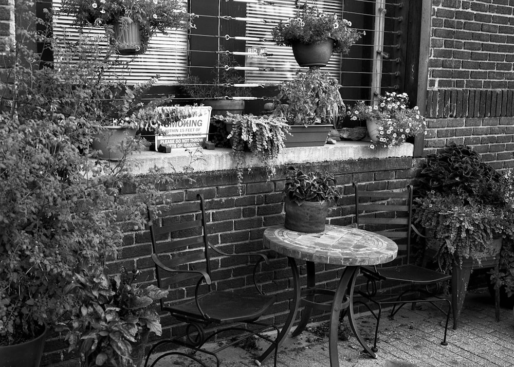 a black and white photo of a table and chairs in front of a brick building