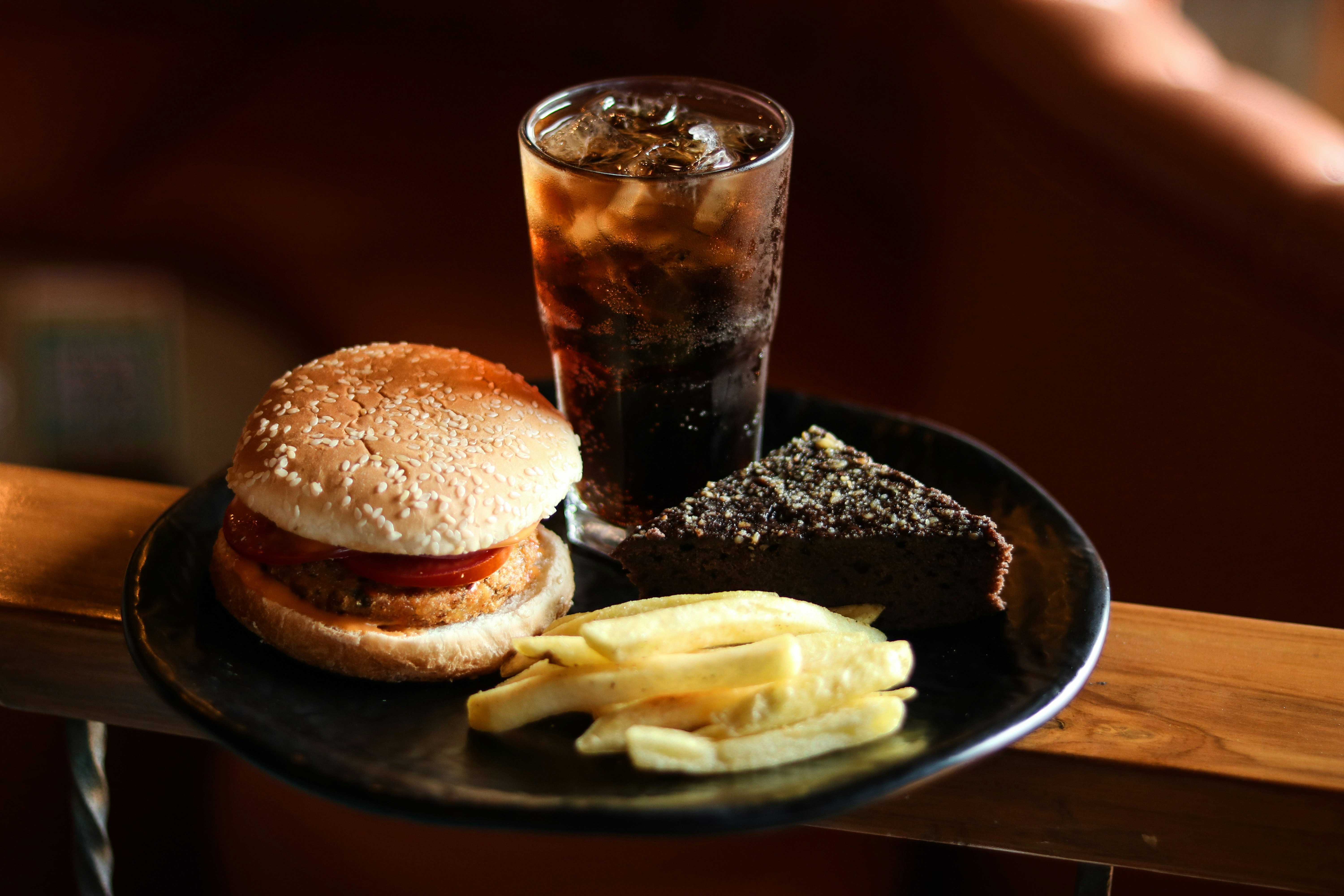 Burger fries cola and cake on a dining plate.
