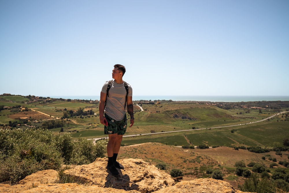 a man standing on top of a mountain next to a lush green valley