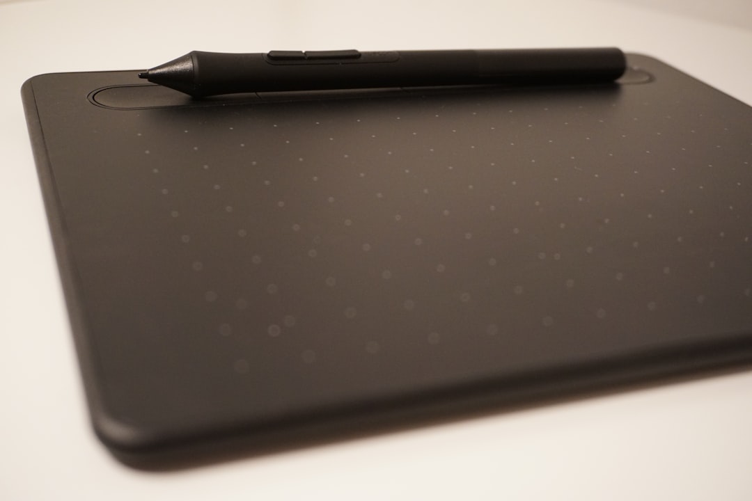 a pen sitting on top of a black tablet, A black pen sitting on top of a black drawing tablet.