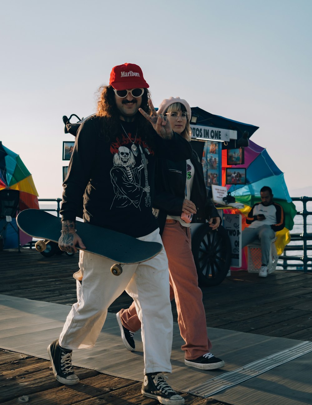 a man and woman walking on a boardwalk with a skateboard