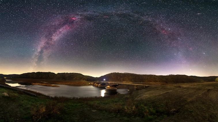 A serene shot of the Milky Way arching over a rugged Australian outback landscape at dusk.