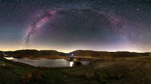 A time-lapse style capture of the Milky Way arching over a quiet creek lined with eucalyptus trees.